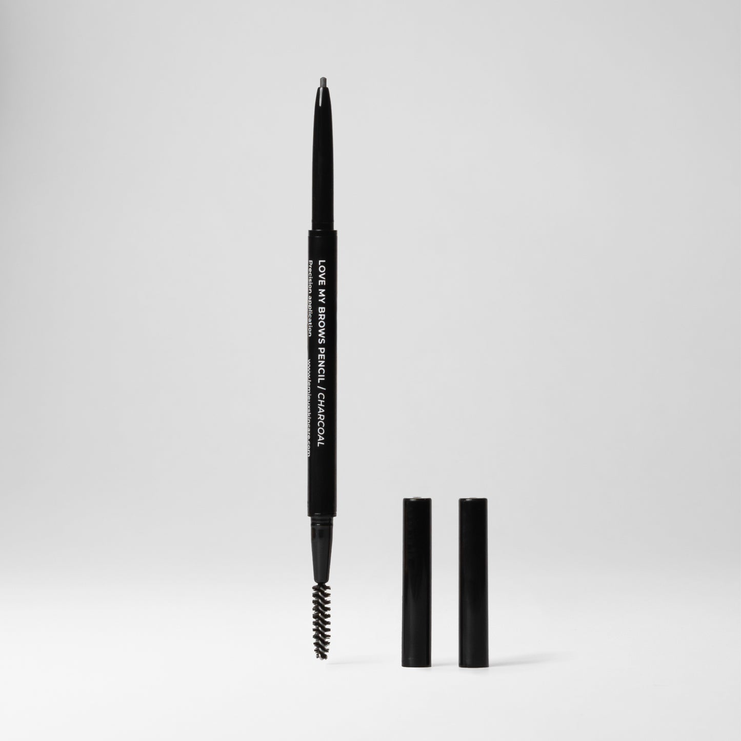 Charcoal Brow Pencil uncapped on both ends with brow pencil on top and brush on the bottom. Caps of both ends standing next to it. All in front of a light grey background.