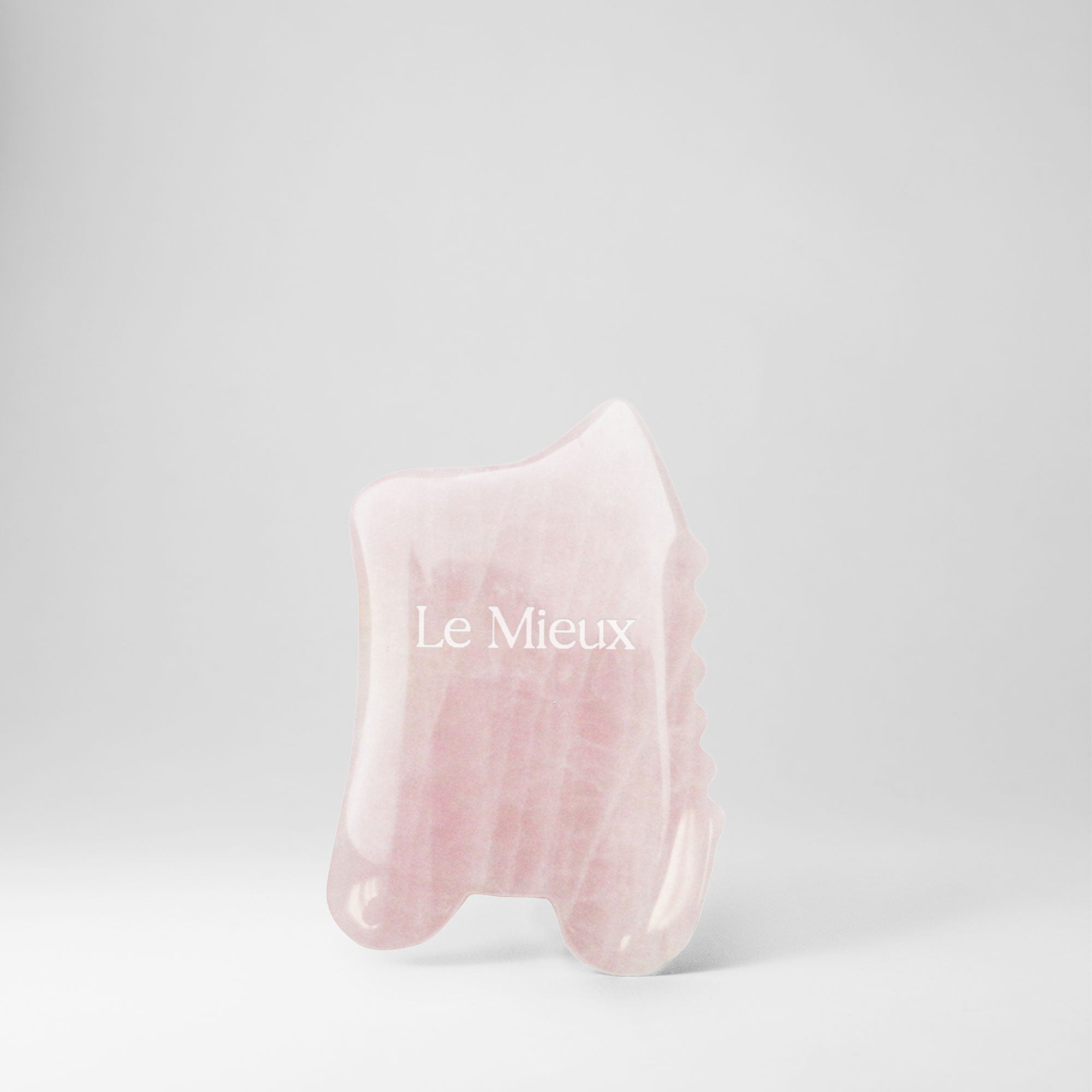 Light pink Gua Sha with "Le Mieux" on it isolated on a light grey background