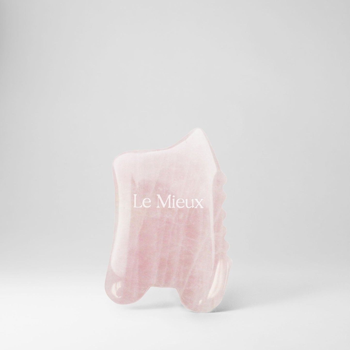 Light pink Gua Sha with "Le Mieux" on it isolated on a light grey background 
