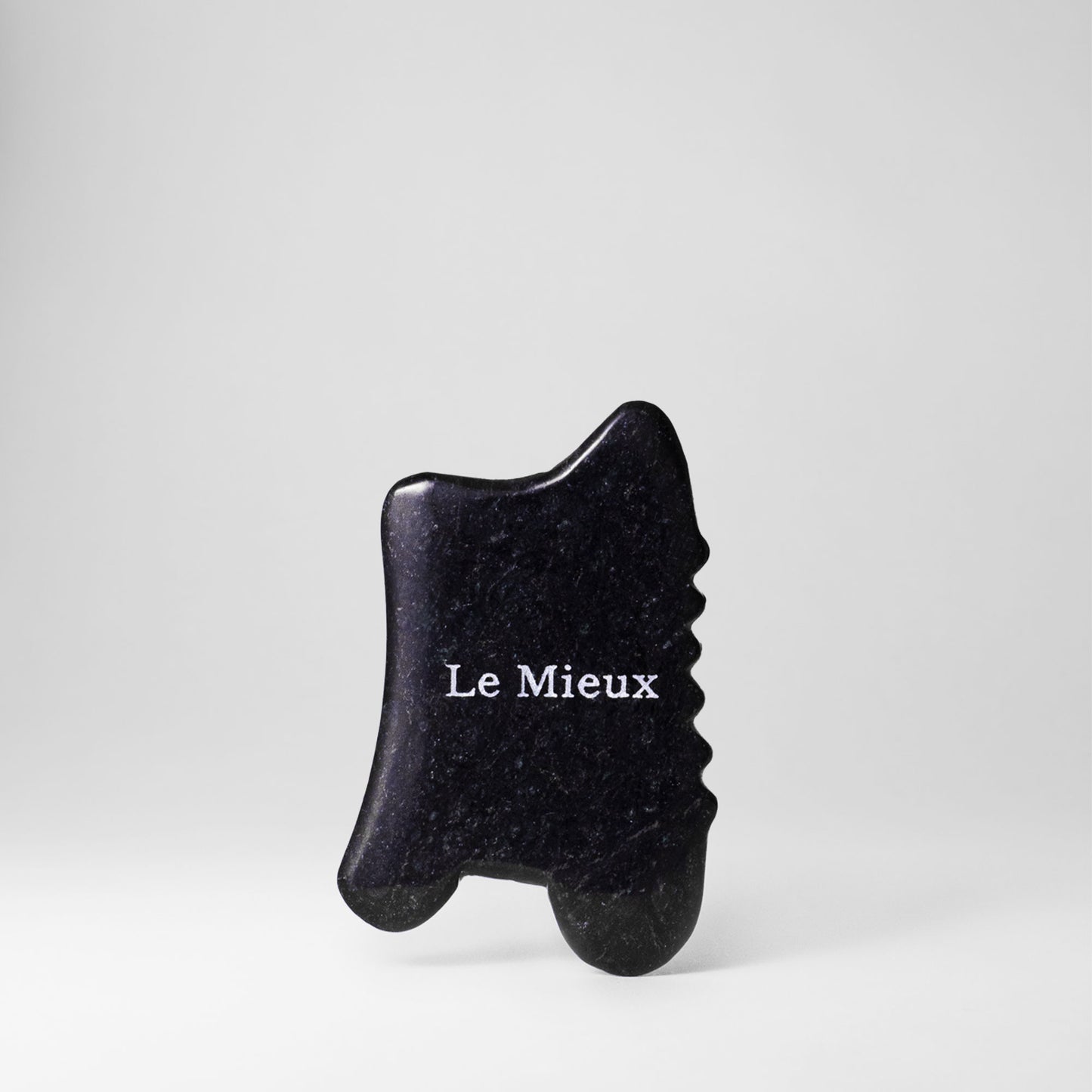 Black Gua Sha with "Le Mieux" on it isolated on a light grey background 