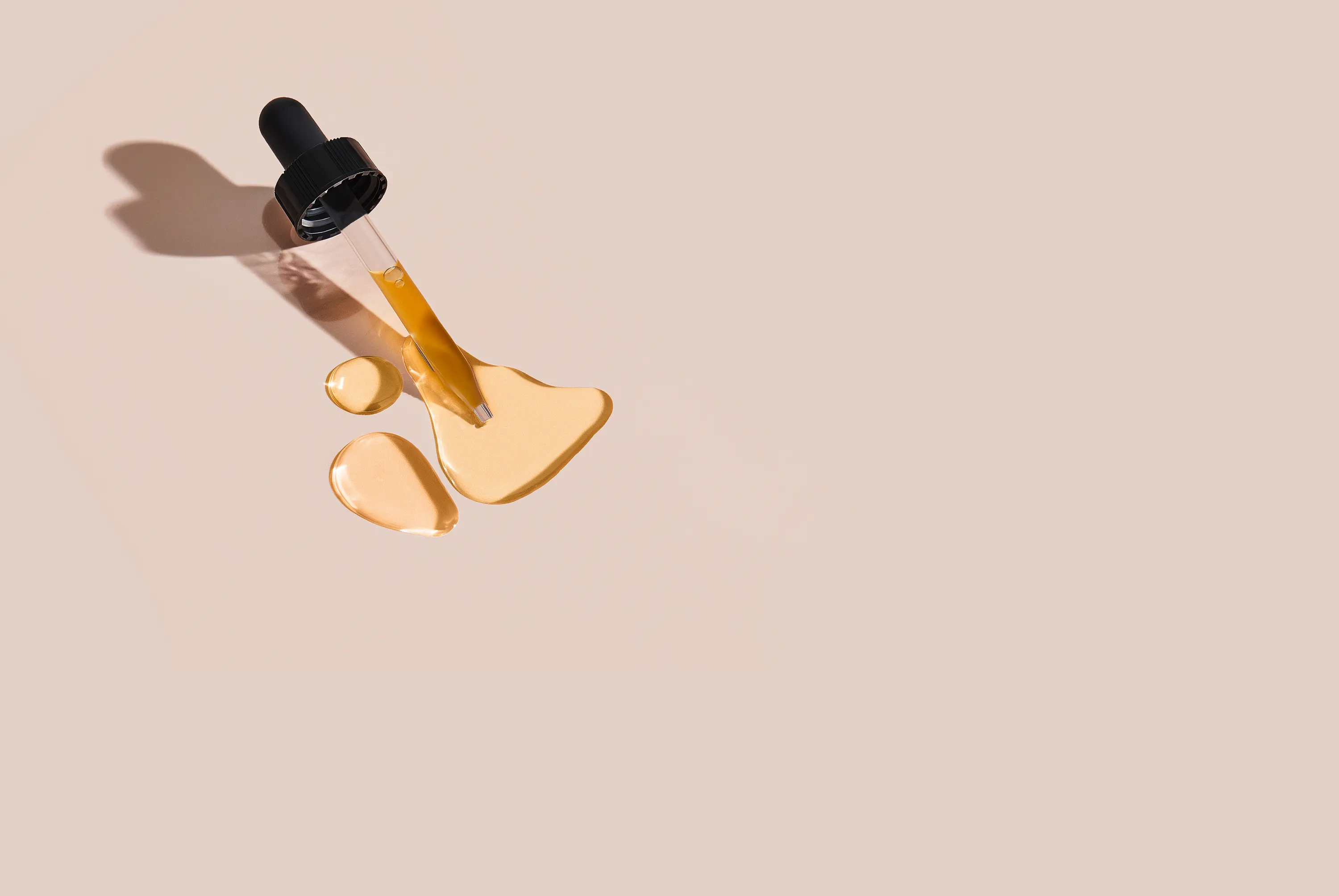 dropper with orange liquid pooling under it on a light beige background