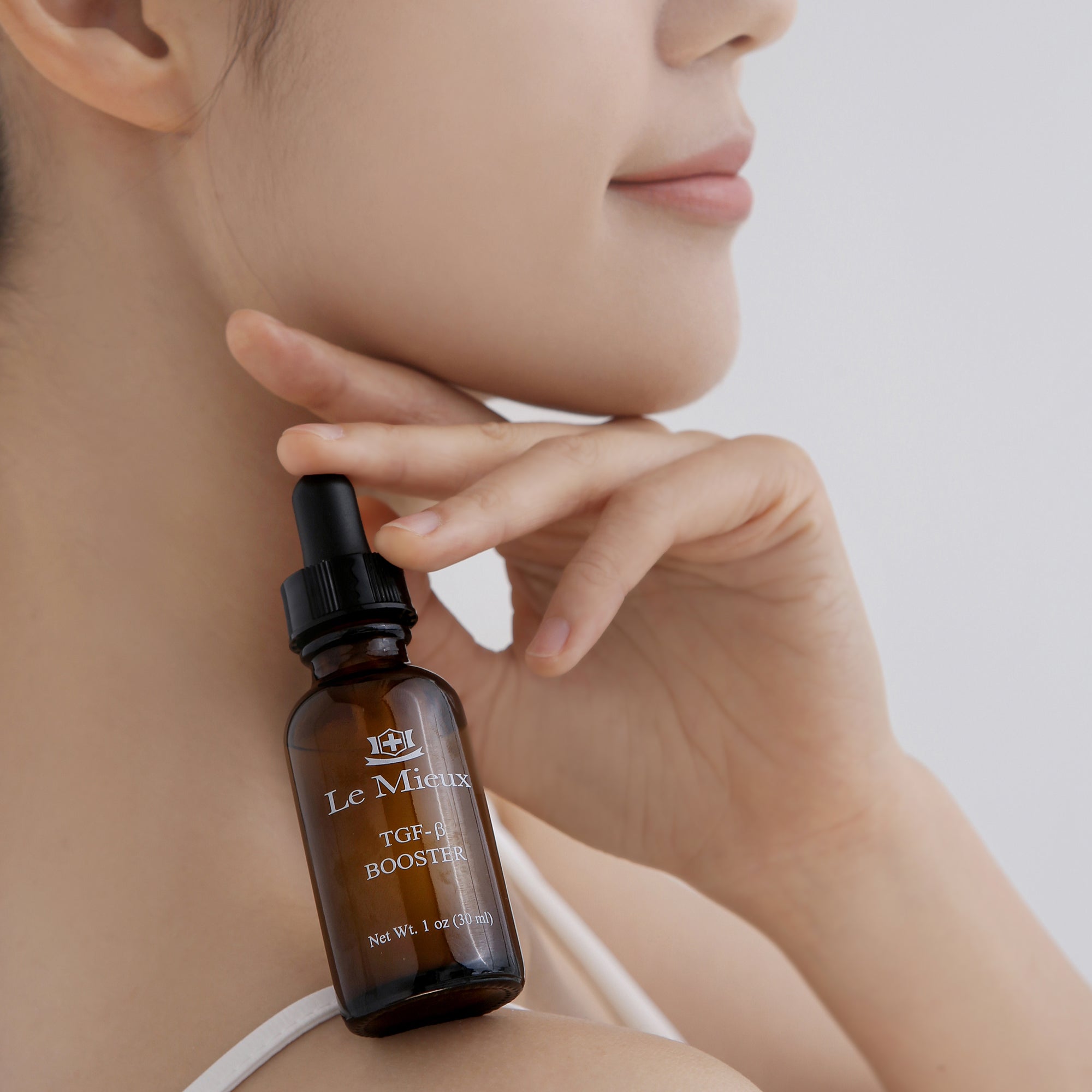 woman holding an amber TGF-β Booster bottle on her shoulder with her hand in front of a light gray background