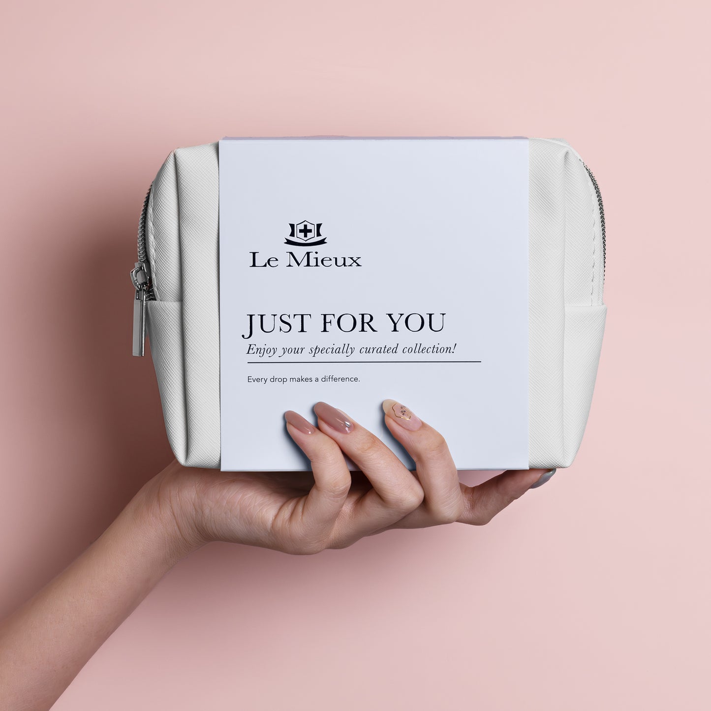 Hand holding white bag with silver zipper and light blue sleeve that says Just for You with Le Mieux logo in front of a pink background.