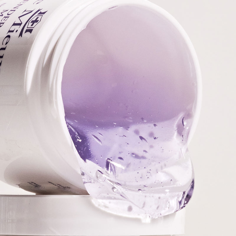 A lidless Lavender Floral Mask container on its side with light purple gel mask spilling out of it in front of a light grey background.