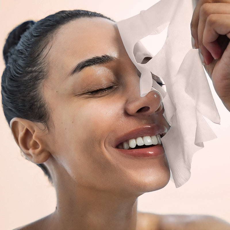 Smiling woman with eyes closed peeling off a white mask from her face.