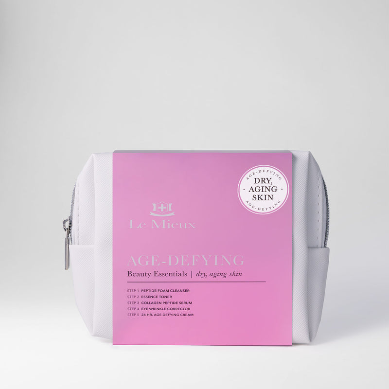 White bag with silver zipper and pink sleeve that says Age-Defying Beauty Essentials with Le Mieux logo in front of a light gray background.