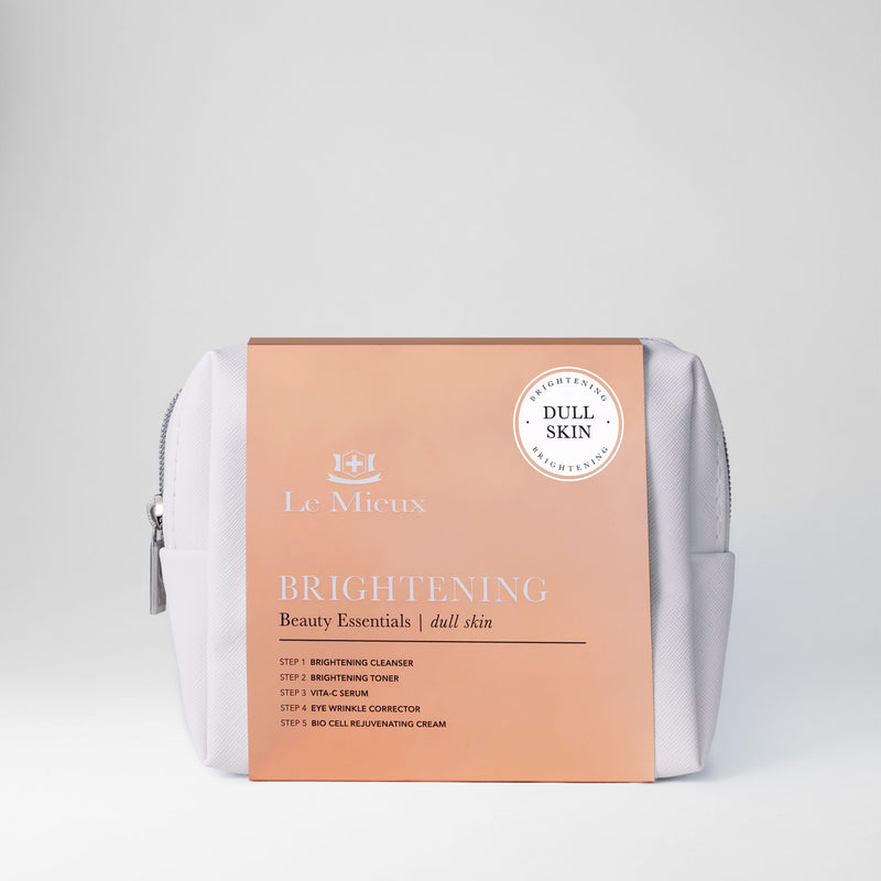 White bag with silver zipper and orange sleeve that says Brightening Beauty Essentials with Le Mieux logo in front of a light gray background.