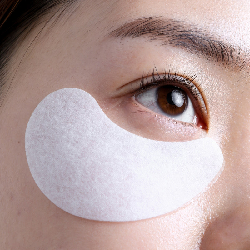 Close up of a singular white Eyelift Mask placed under woman's eye as she looks up.