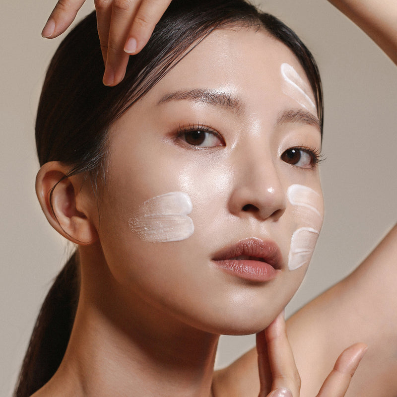 Woman with white exfoliant textures on both cheeks and on the side of her forehead.